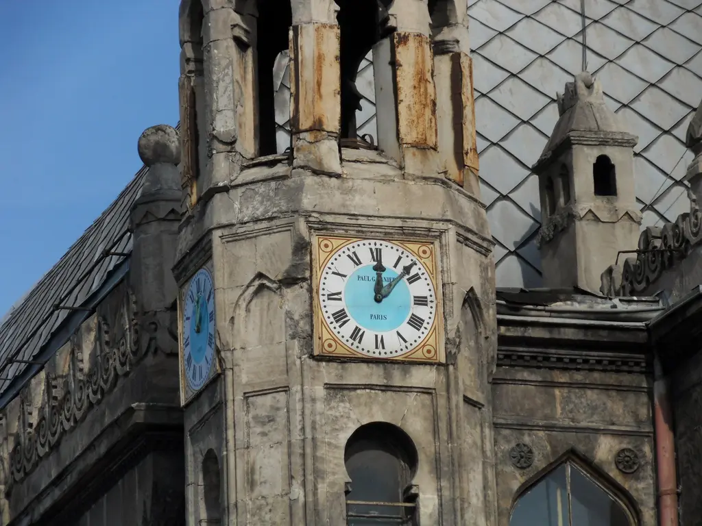 Sirkeci Garı'nın saat kulesi yakın planda; beyaz mineli kadranda romen rakamları ve Paris imalatçı damgası, yanda turkuaz kadranlı ikinci saat, arkada elmas desenli cam kubbe.