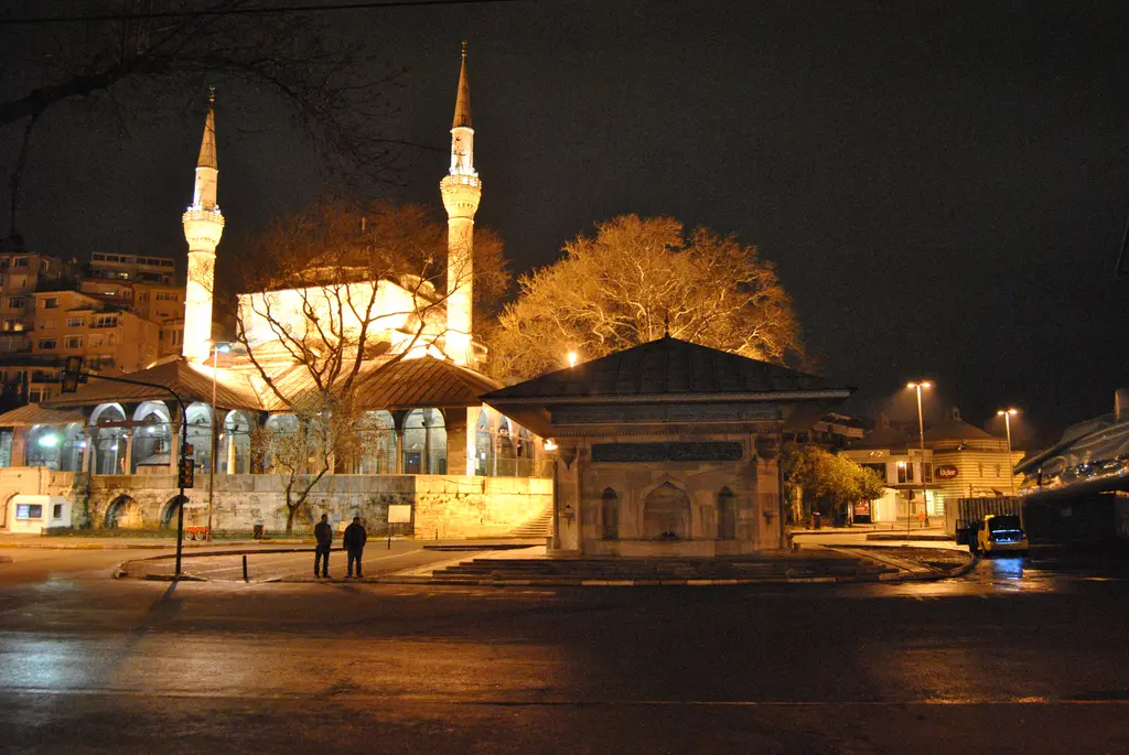 Gece Mihrimah Sultan Camii; ışıklı kubbe ve minareler, önünde aydınlatılmış ağaçlar ve meydandaki çeşme.