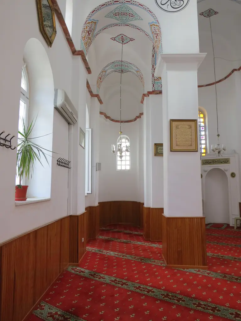 Bodrum Camii'nin yan nefi; beşik tonozlu bölüm, kalem işi bordürler, kemerli pencere, ahşap lambri, çerçeveli hat levhaları ve kırmızı halı.