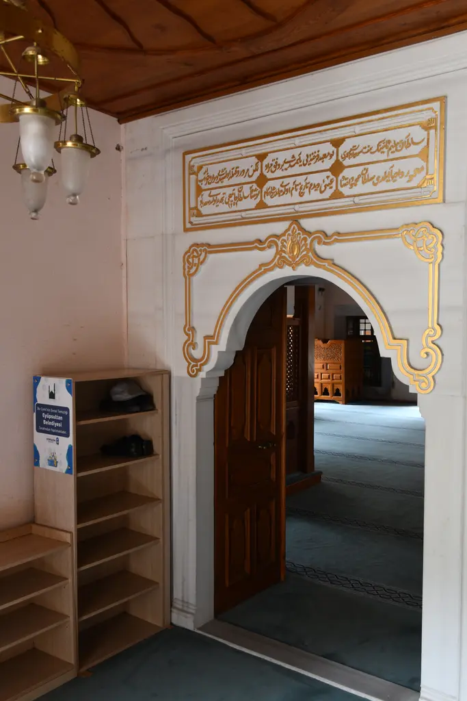 Şah Sultan Camii'nin harim kapısı; yaldızlı kitabe, kıvrımlı alçı süslemeli kemer, ahşap kapı ve yanında ayakkabılık.