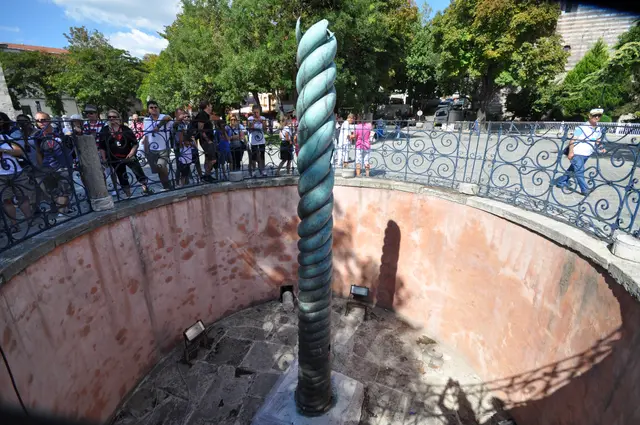 Sultanahmet Meydanı'nda Yılanlı Sütun; pembe sıvalı yuvarlak çukurun ortasında yeşil patinalı burmalı tunç gövde, üstte parmaklık ve kalabalık.