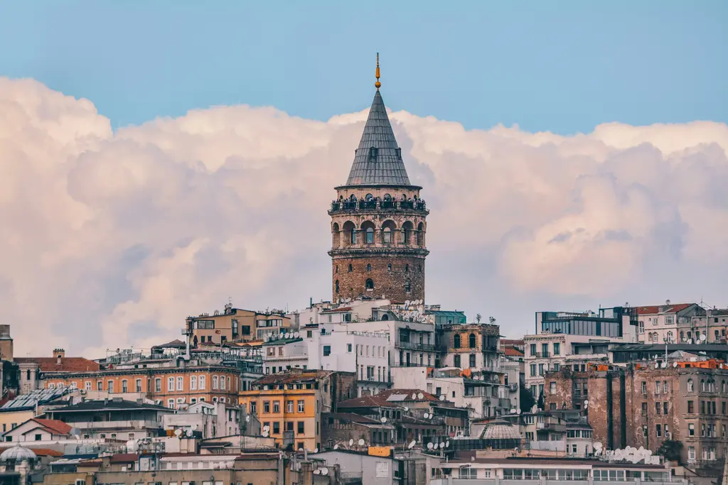 Beyoğlu'nda Galata Kulesi; konik külahlı taş gövdesi, çevresini saran çok katlı apartmanlar ve arkada pembe tonlu bulutlar.