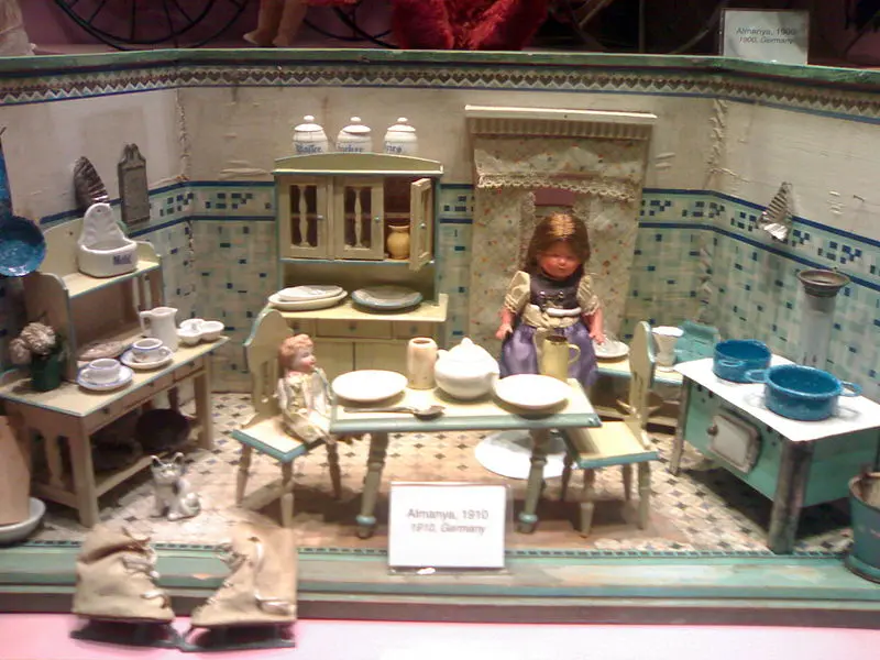 İstanbul Oyuncak Müzesi'nde bebek evi mutfağı; çinili duvar, minik ocak, tabaklar, tencereler ve masada oturan bebek.