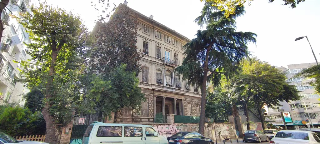 Moda'da Sarıca Arif Paşa Konağı; taş cepheli büyük yapı, ağaçlar, sokak ve önde park etmiş araçlar.