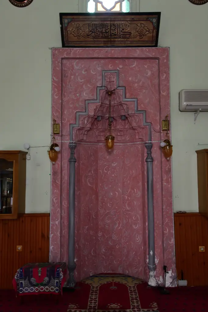 Defterdar Camii'nin mihrabı yakından; pembe mermer niş, mukarnas başlık, şamdanlar ve önünde seccadeler.
