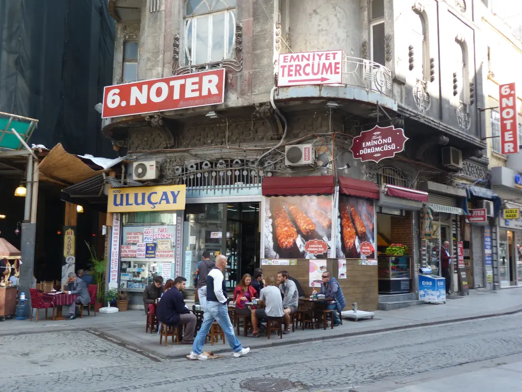 Eminönü'nde köşedeki dürümcü; tabelalar, dükkân önünde masalarda oturanlar ve üst katlarda noter ve tercüme tabelaları.