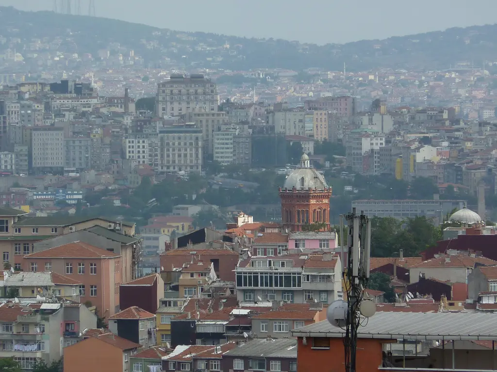 Yüksekten şehir manzarası; ortada okul binası, çevresinde Fener'in çatıları, arkada Haliç ve karşı yaka.