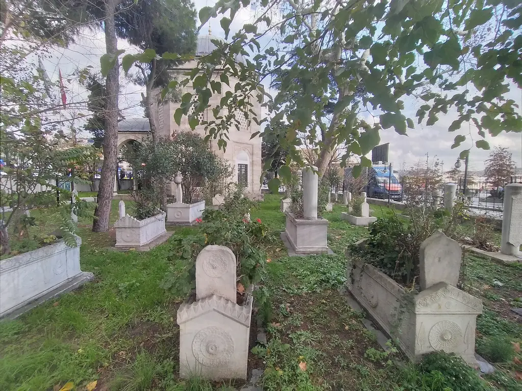 Barbaros Hayreddin Paşa Türbesi'nin haziresinde mezar taşları; çimenler, ağaçlar ve arka planda türbenin taş gövdesi.