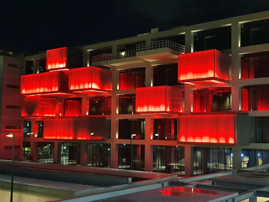 Gece İstanbul Resim ve Heykel Müzesi; cephede kırmızı ışıklı kutular, katlı beton taşıyıcılar ve önde kıyı.