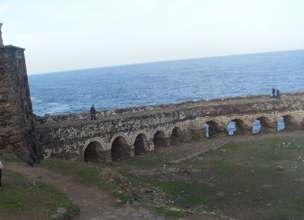 Rumeli Feneri Kalesi'nde kemerli sur; denize doğru uzanan taş kemerler, üzerinde yürüyen insanlar ve mavi deniz.