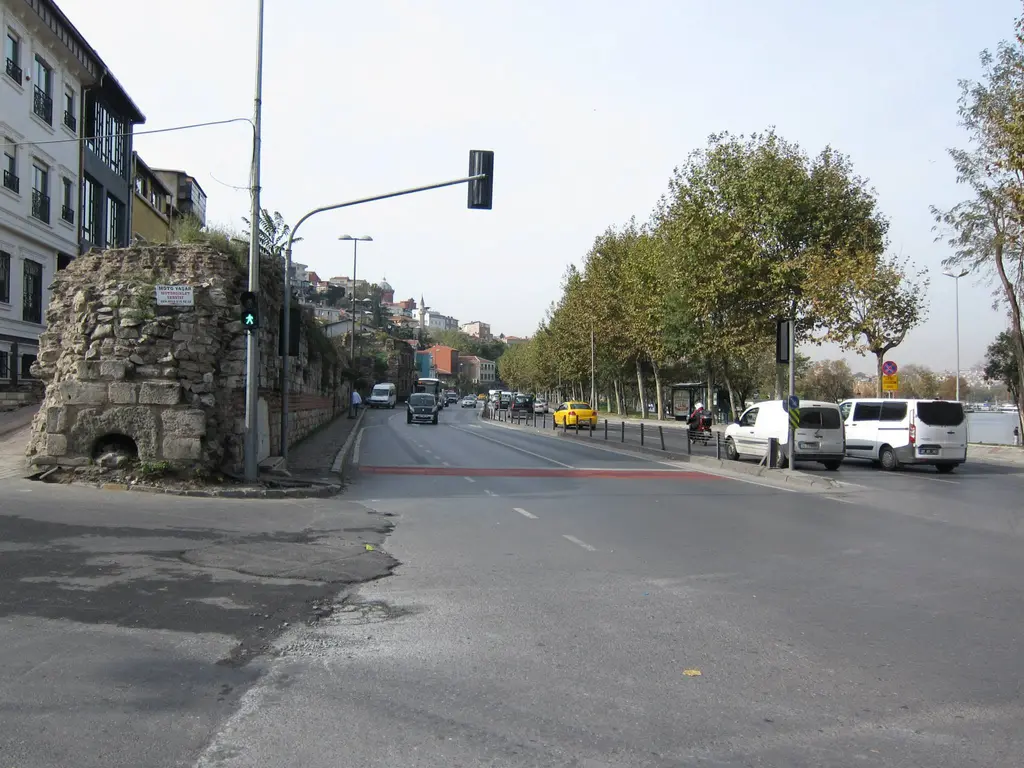 Abdülezelpaşa Caddesi; solda yıkık sur kalıntısı, yokuş sokak, trafik ışığı, ağaçlar ve park etmiş arabalar.