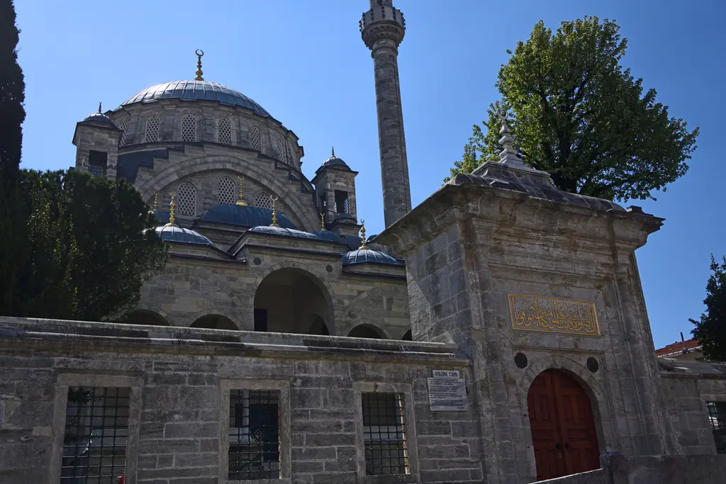 Ayazma Camii'nin avlu kapısı; kemerli kırmızı kapı ve üstünde kitabe, arkada kubbeler ve minare.