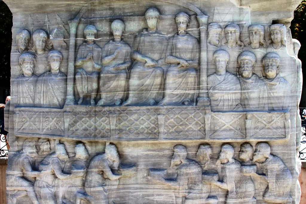 Dikilitaş kaidesinin batı yüzü; üstte locada imparator ve maiyeti, altta diz çöken ve ellerinde sunular taşıyan figürler.