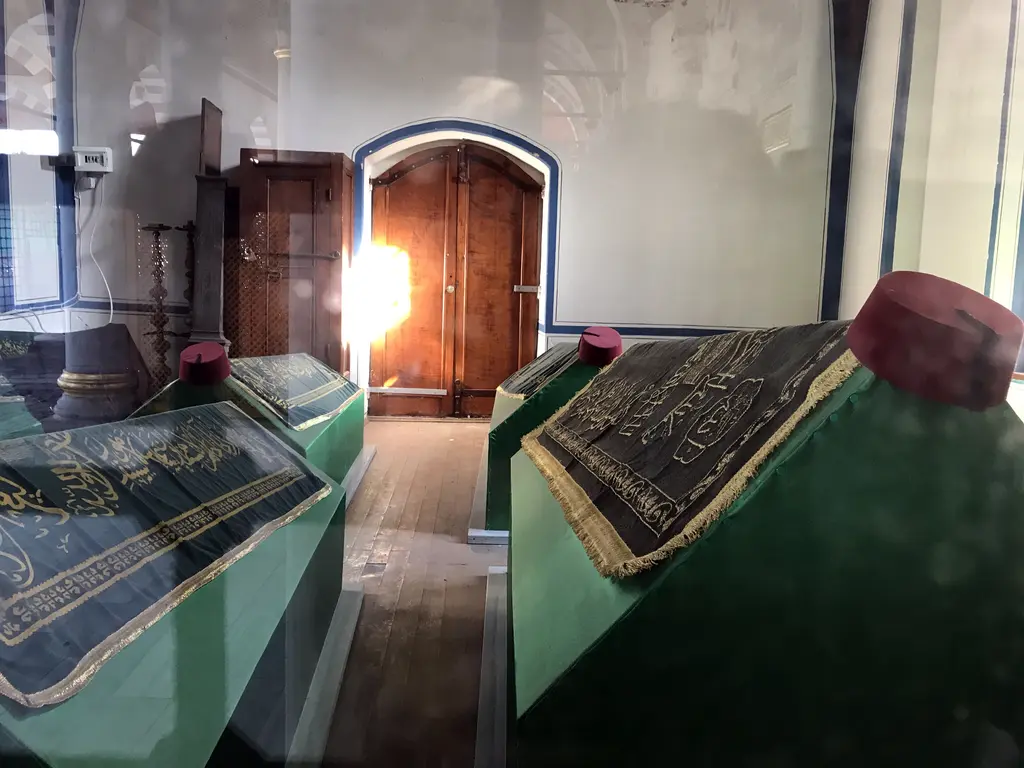 İbrahim Edhem Paşa Türbesi'nin içi; yeşil örtülü mermer sandukalar, ahşap kapı ve demir şebekeli pencereler.