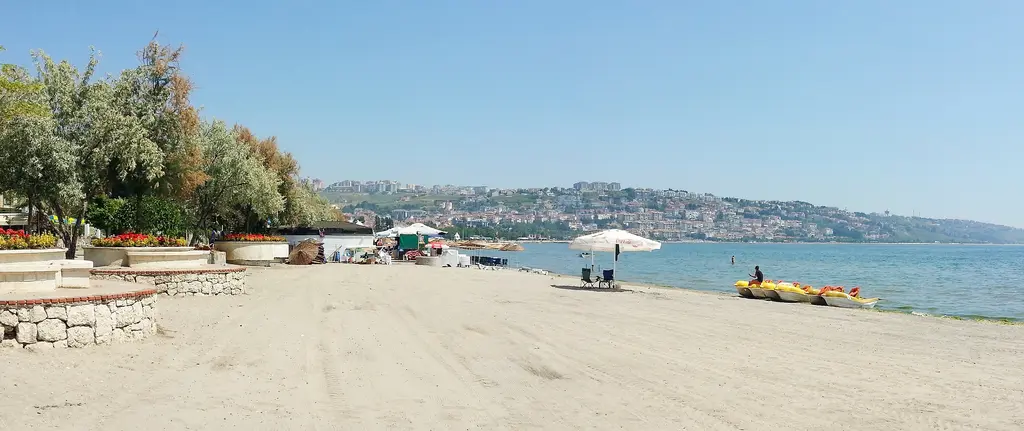 Büyükçekmece kumsalı; geniş kum şeridi, sahilde ağaçlar ve şemsiyeler, uzakta kıyı boyunca yerleşim.