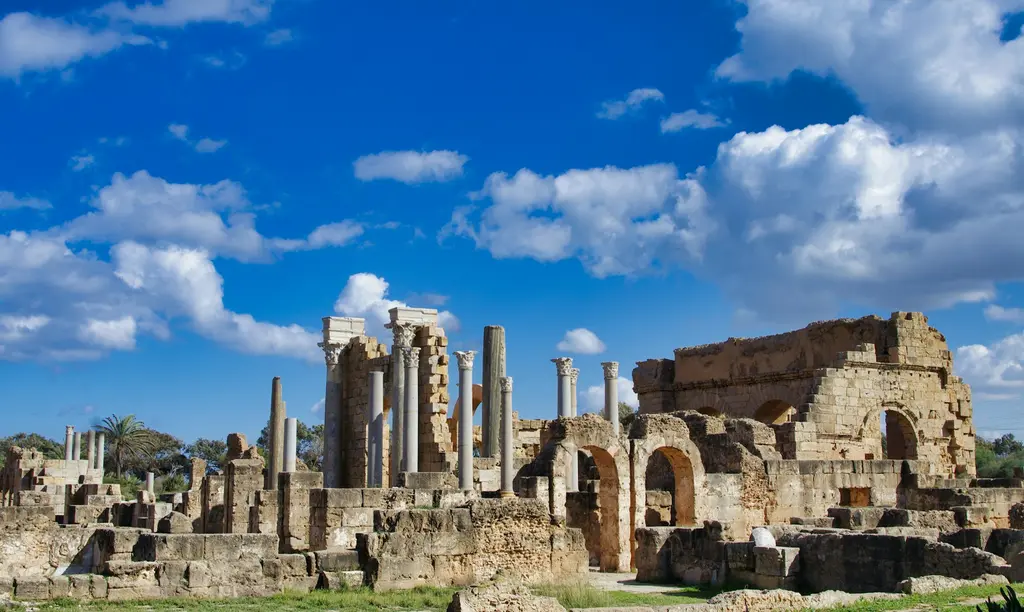 Libya'da Leptis Magna antik Roma kenti; ayakta kalan sütunlar, kemerli duvar kalıntıları ve beyaz bulutlu mavi gökyüzü.