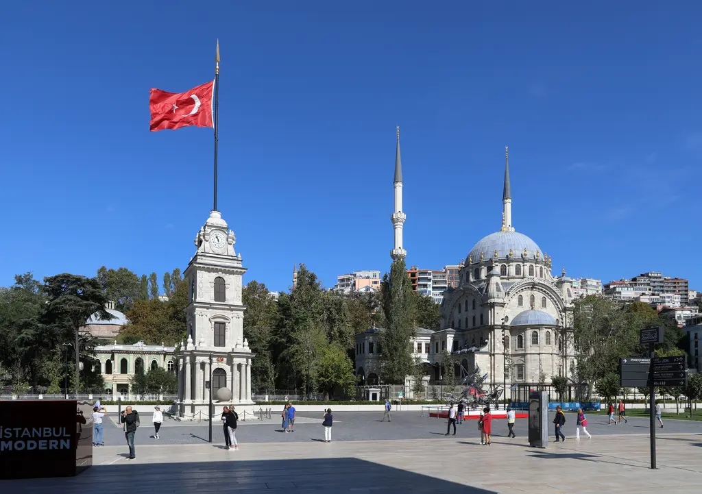 Tophane'de saat kulesi ile Nusretiye Camii; öne çıkan kulenin süslü taş gövdesi, arkada kubbe ve ince minare.