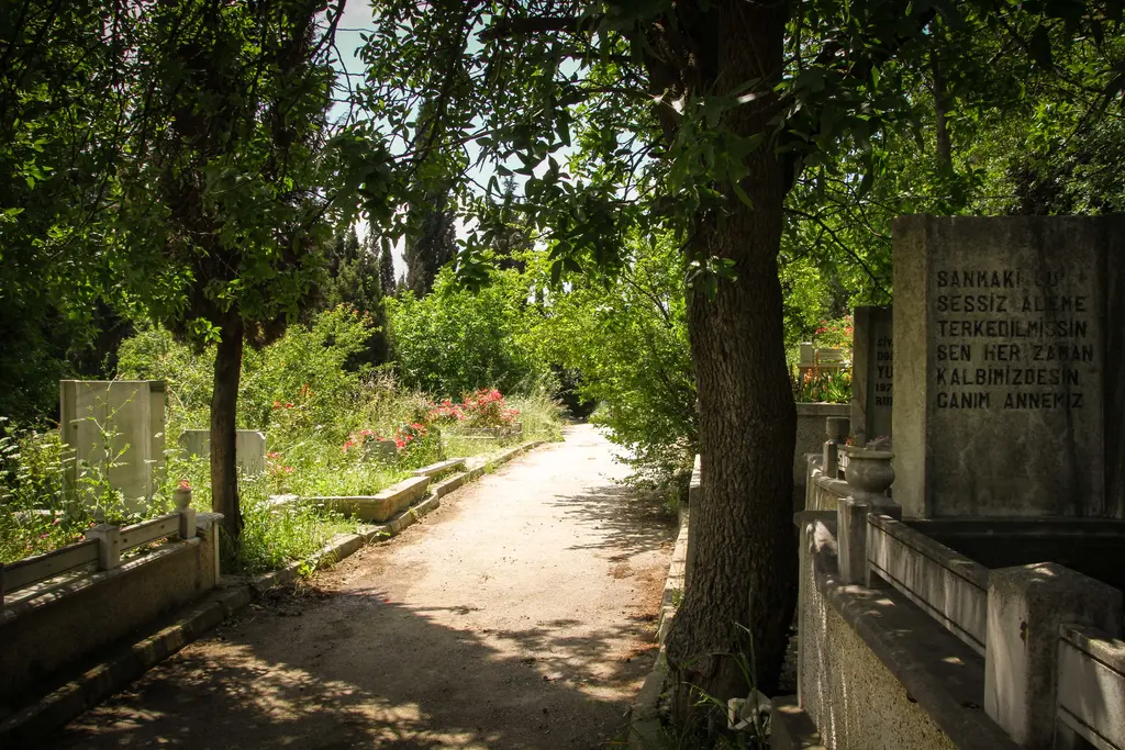 Karacaahmet Mezarlığı'nda dar yol; bir yanda yüksek mezar taşları ve duvar, öte yanda kabirler ve ağaçlar.