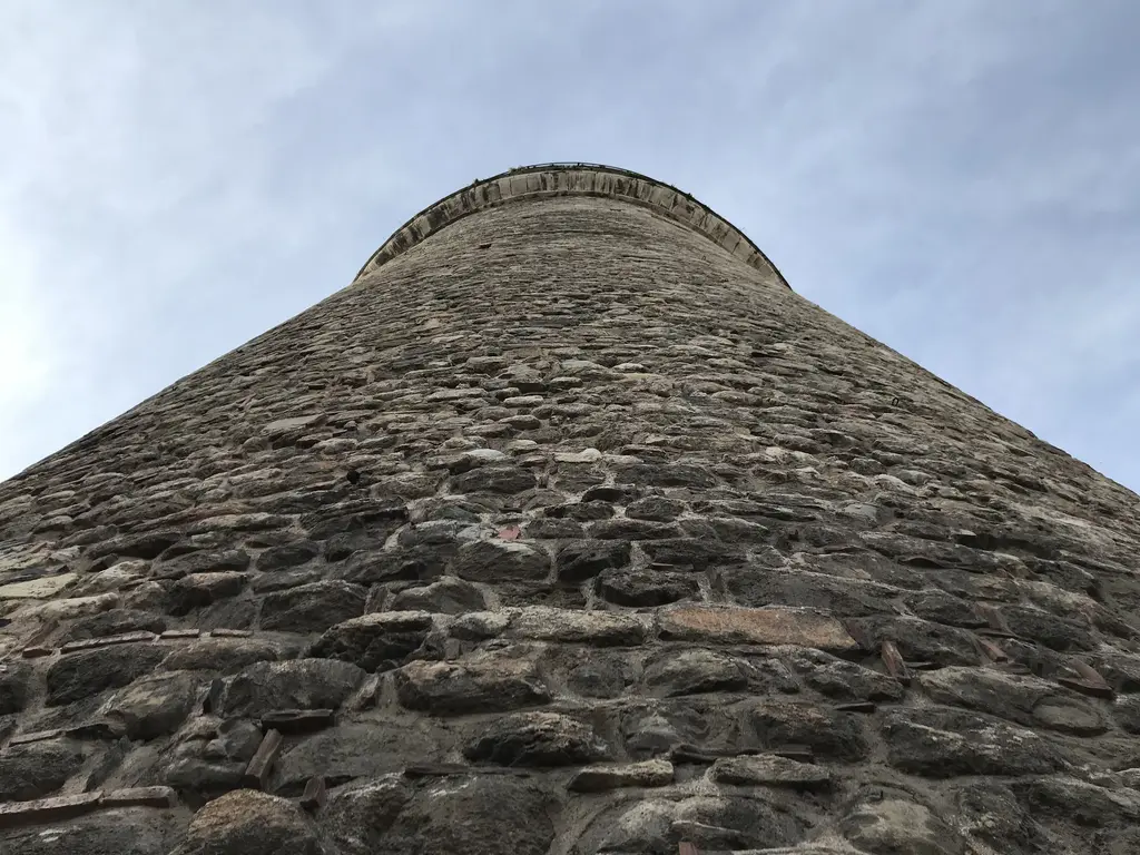 Aşağıdan Galata Kulesi'nin taş gövdesi; kaba yontma taşlarla örülmüş silindir duvar, yukarıda daralan hat ve bulutlu gökyüzü.