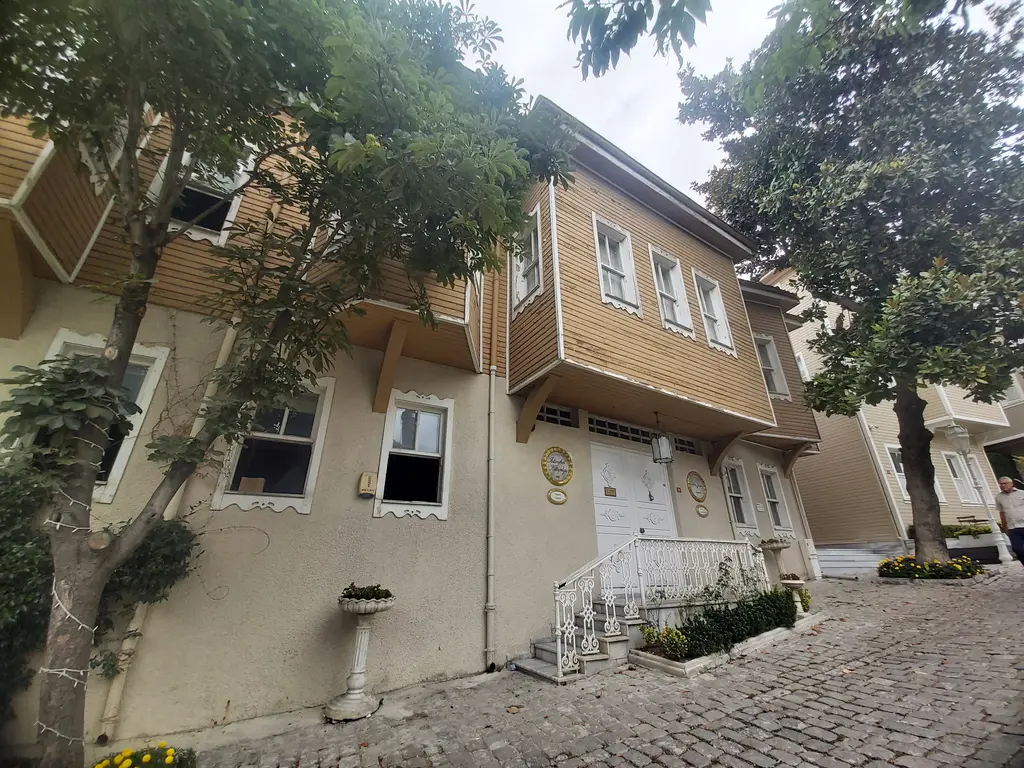 Soğukçeşme Sokağı'nda İstanbul Kitaplığı'nın bej boyalı ahşap binası; beyaz korkuluklu giriş merdiveni, yanında ağaçlar ve taş döşeli yol.