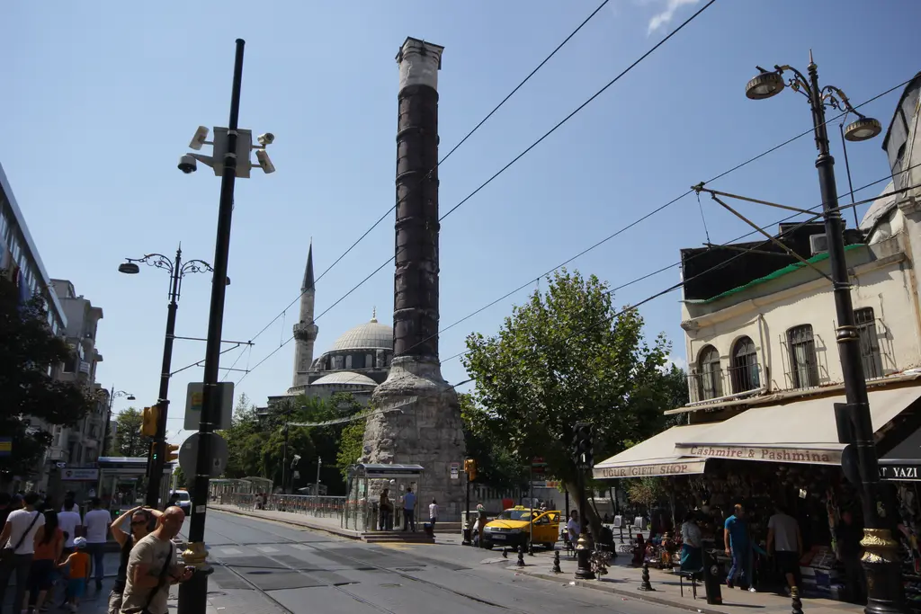 Çemberlitaş'ta Divanyolu; caddenin iki yanında dükkânlar ve tenteler, ortada yükselen sütun, uzakta bir minare.