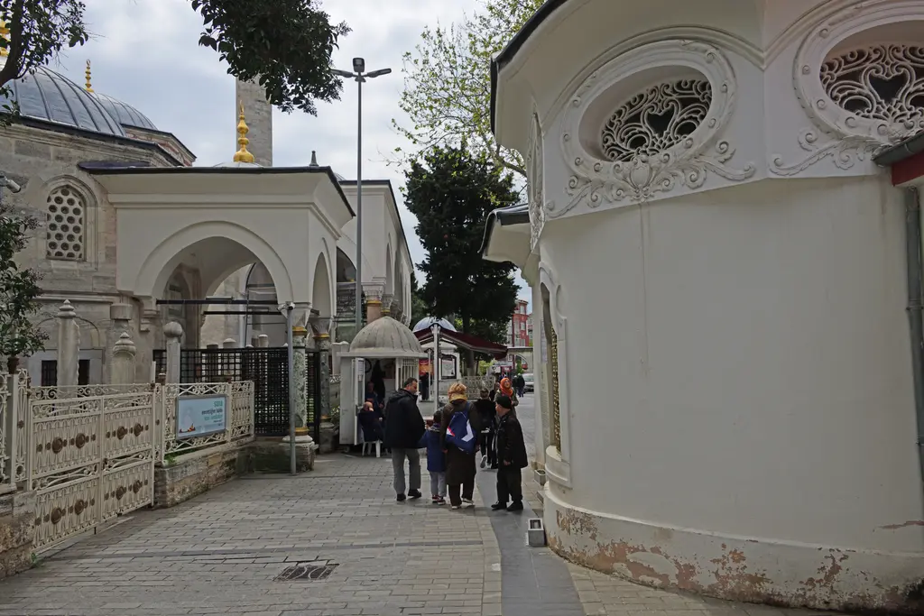 Koca Mustafa Paşa Külliyesi'nde türbe ile cami arasındaki dar avlu; sağda oval madalyon kabartmalı beyaz türbe duvarı, solda kemerli açık türbe ve mermer korkuluk, arkada minare.