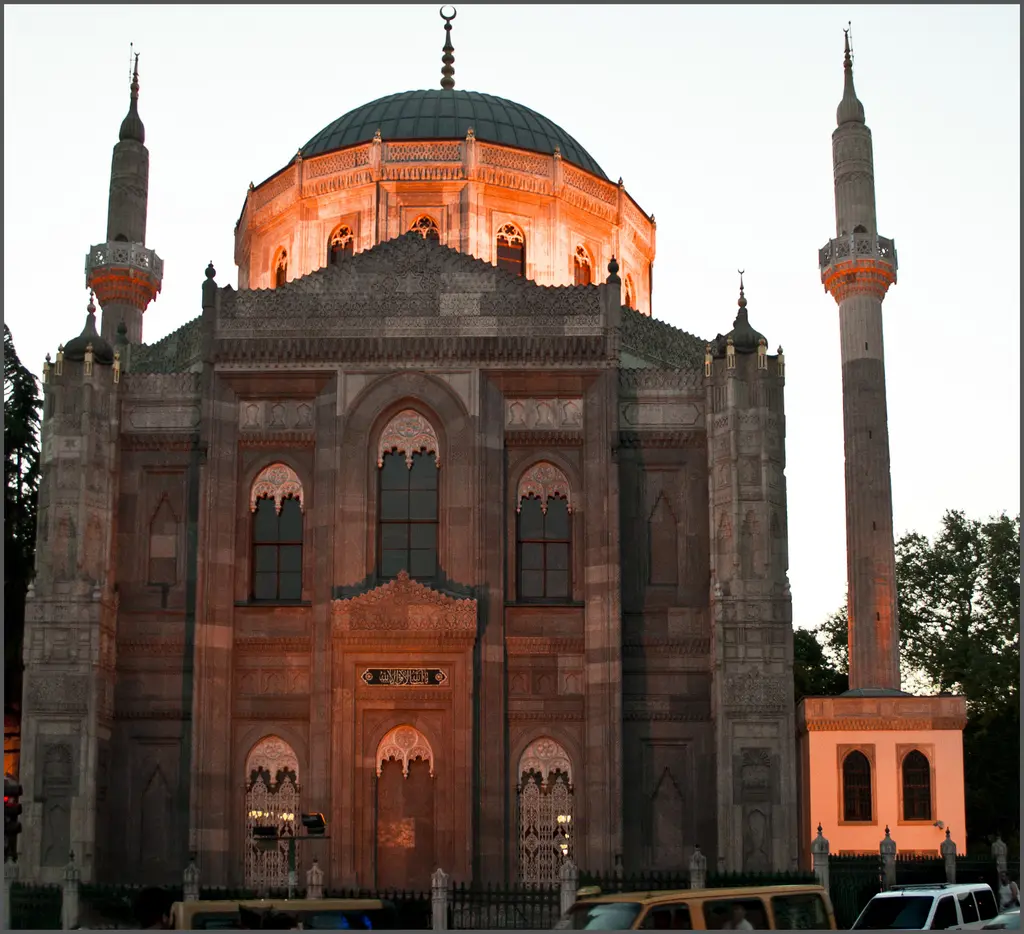 Gün batımında Pertevniyal Valide Sultan Camii; kızıl ışık alan taş cephe, turuncu parlayan kubbe, iki minare ve koyu gökyüzü.