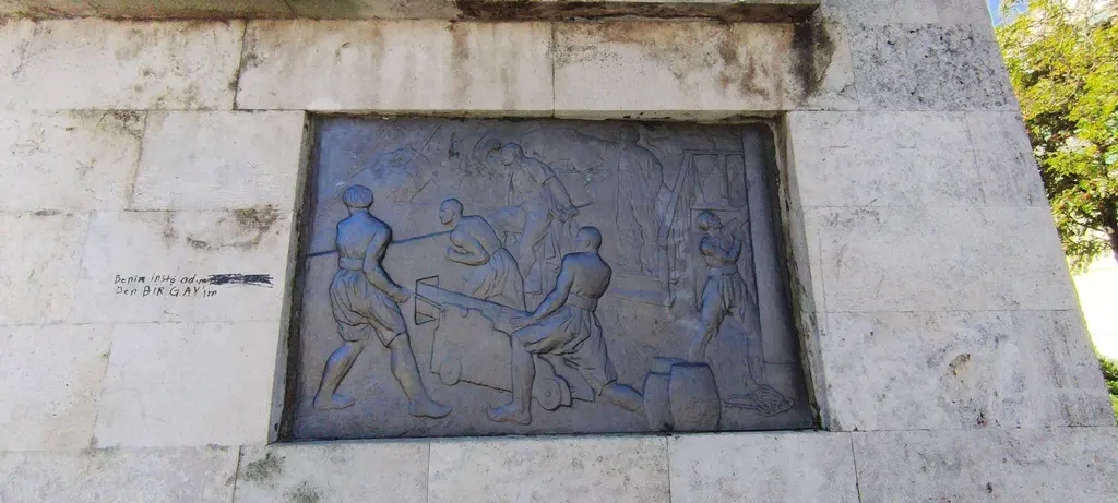 Barbaros Anıtı'nın kaidesinde bronz kabartma; taş duvara gömülü dikdörtgen pano ve üzerinde hareketli figürler.