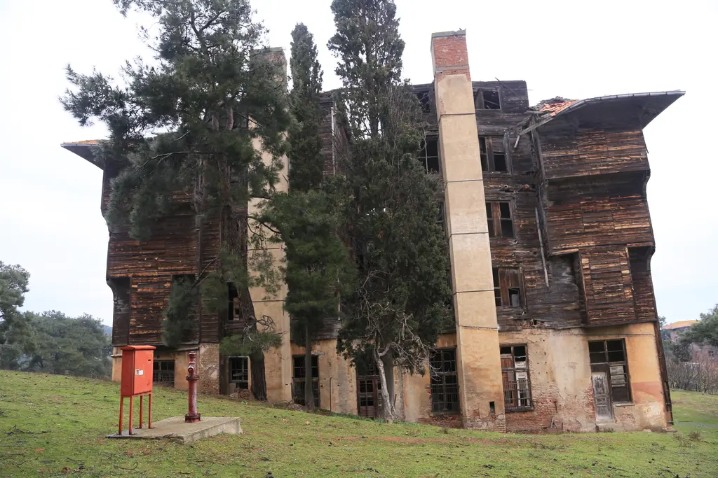 Büyükada'da Rum Yetimhanesi; ağaçların arasında yükselen dev, harap ahşap bina ve çökmüş kat pencereleri.