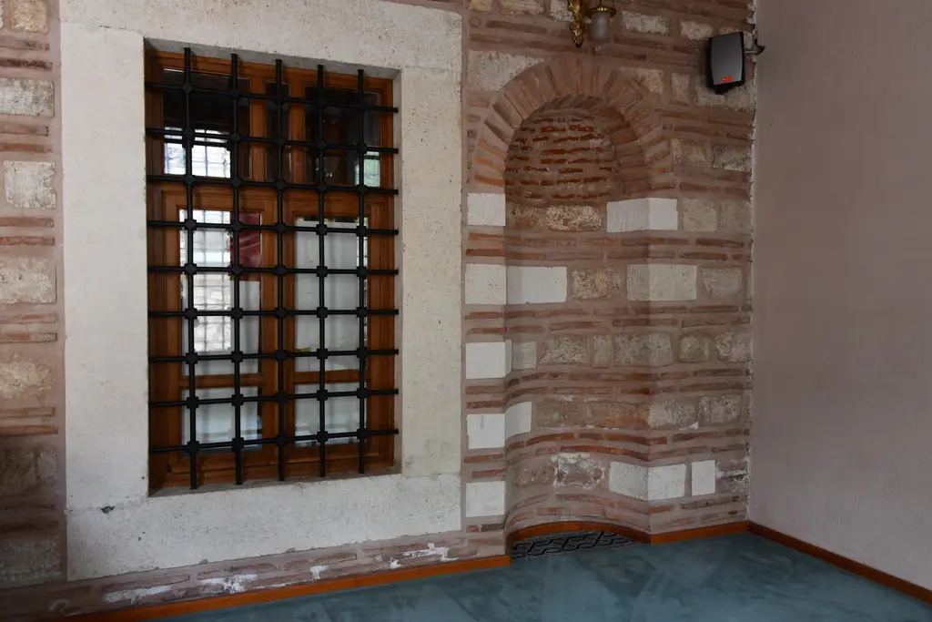 Şah Sultan Camii'nin iç duvarı; tuğla ve taş sıralı açıkta bırakılmış duvar, demir şebekeli pencere ve kemerli niş.