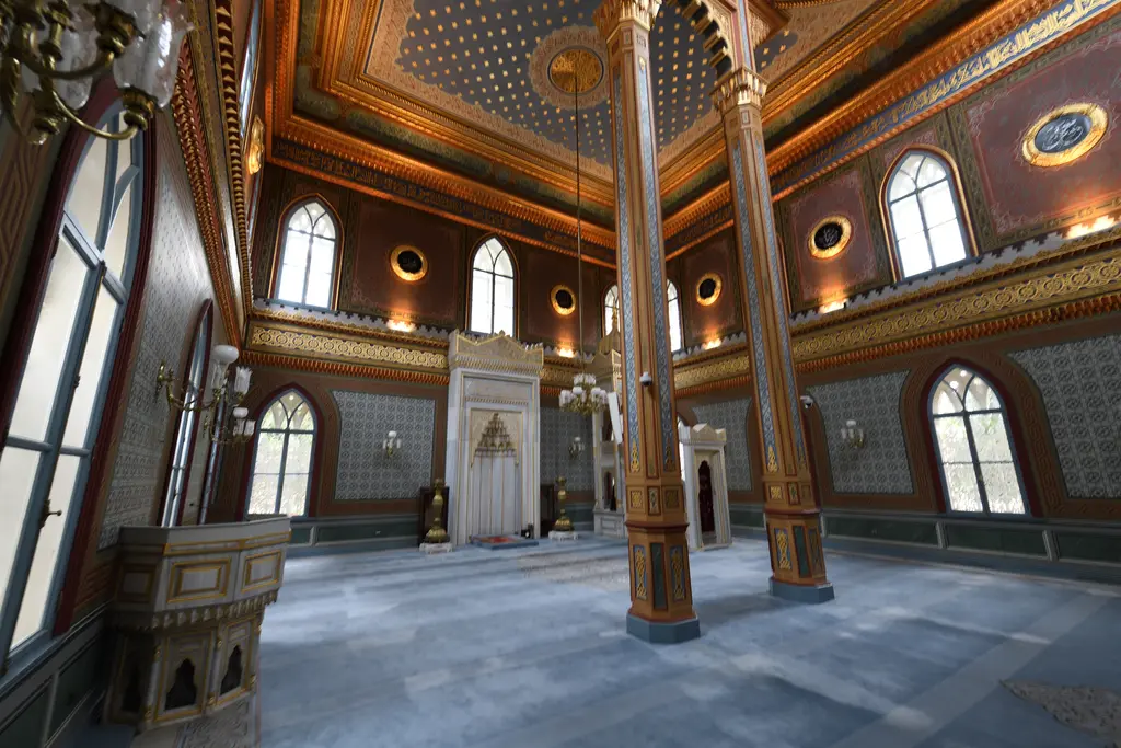 Yıldız Hamidiye Camii'nin harimine çapraz bakış; mermer mihrap, iki ahşap kolon, vaaz kürsüsü ve geniş pencereler.