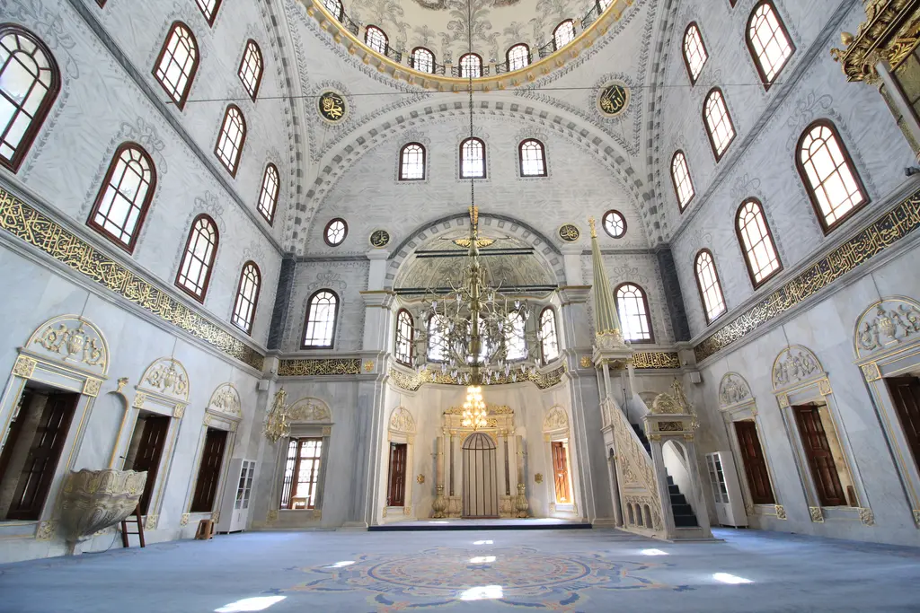 Nusretiye Camii'nin harimi; mavi halı, ortada mihrap, sağda mermer minber, iki yanda kemerli pencere sıraları ve yaldızlı süslemeler.