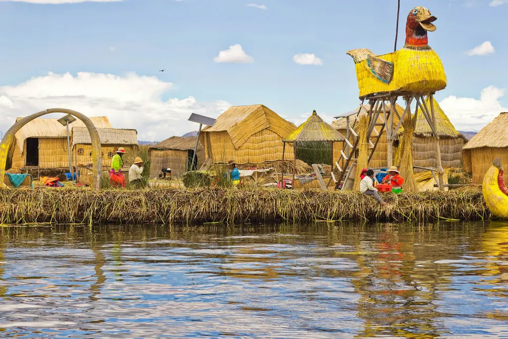 Titicaca Gölü; koyu mavi geniş göl yüzeyi, kıyıdaki sazlıklar ve arkadaki And tepeleri.