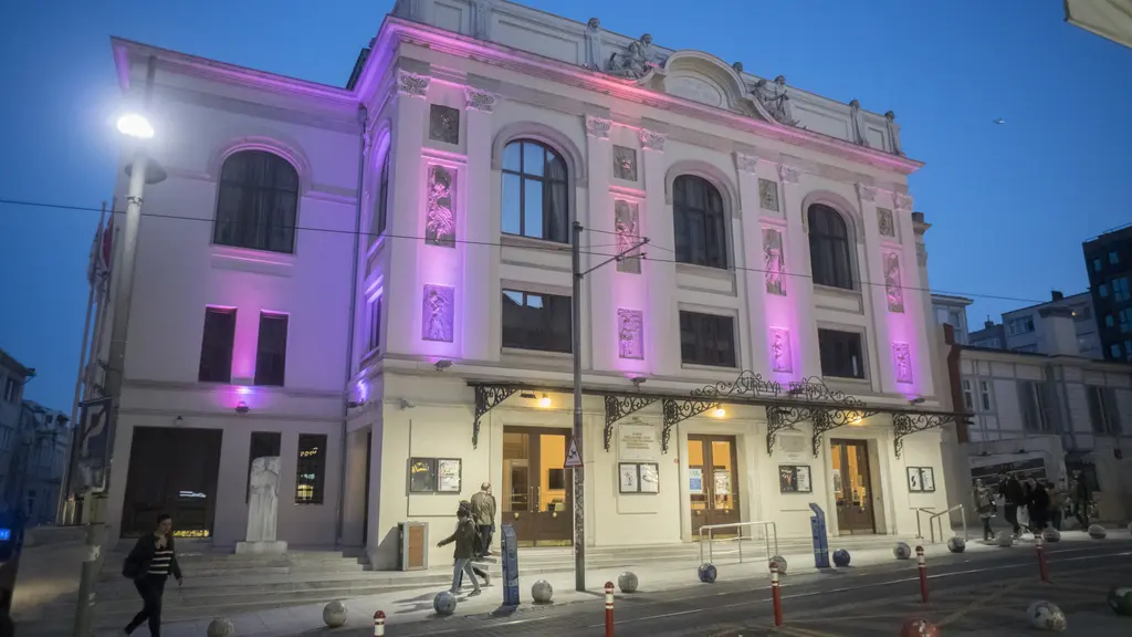 Akşam Süreyya Operası; mor ışıkla aydınlatılmış beyaz cephe, sokak lambaları ve Bahariye Caddesi.