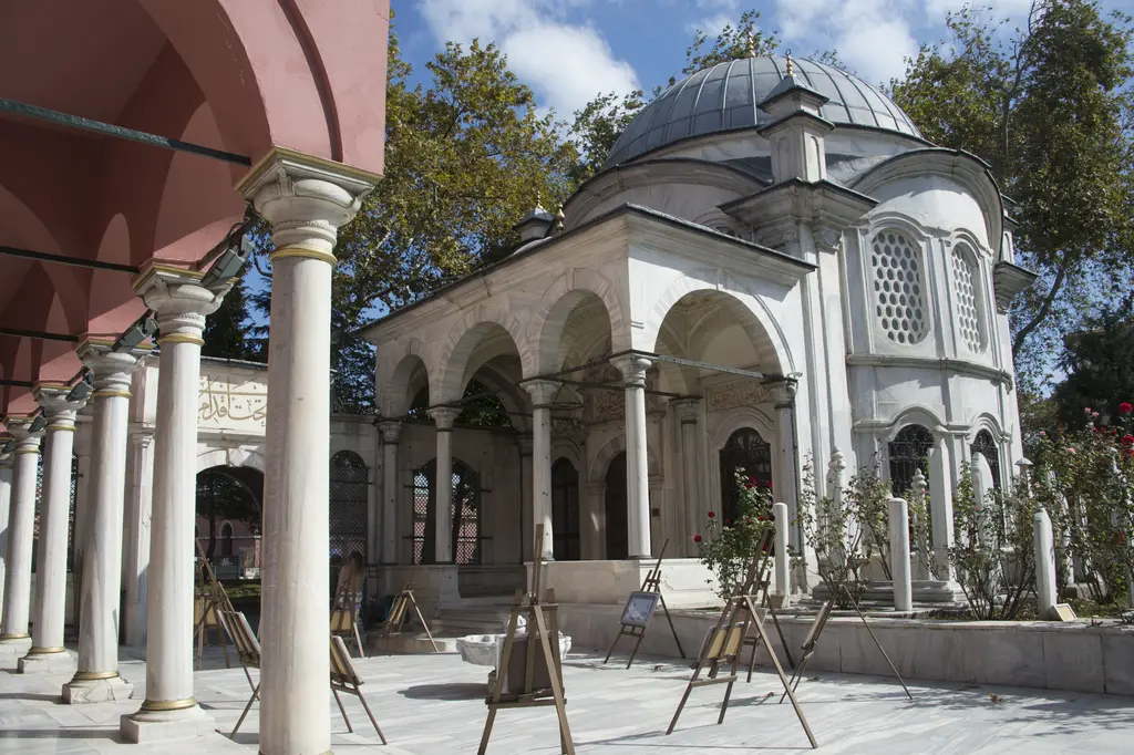 Şah Sultan Külliyesi'nin avlusu; pembe revaklı mektep binası, mermer sütunlar, kubbeli türbe ve sergi şövaleleri.
