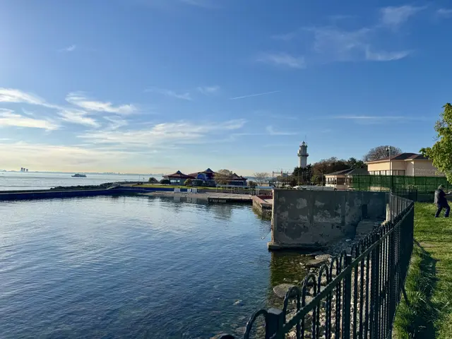 Kadıköy'de Fenerbahçe Parkı; demir korkuluklu kıyı, sakin deniz, uzakta beyaz fener kulesi ve çay bahçesi binaları.