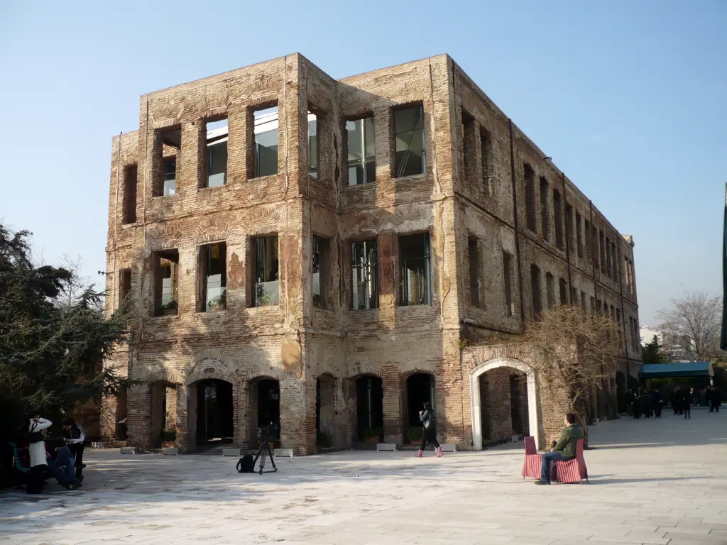 Esma Sultan Yalısı; yanmış tuğla ve taş duvarlar, boş pencere boşlukları, içeride cam yapı ve önde taş döşeli alan.