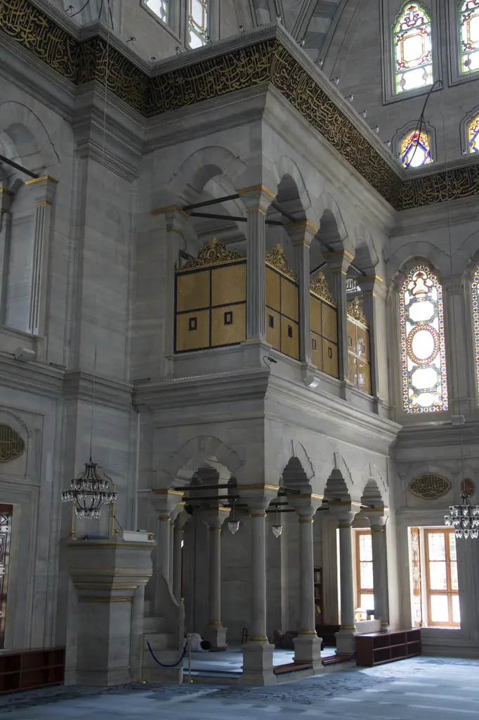 Nuruosmaniye Camii'nde köşe payesinin üstündeki yaldızlı kafesli mahfil; altında kemerli mermer dizi, sağda renkli cam pencere ve yukarıda kalem işli tonoz.