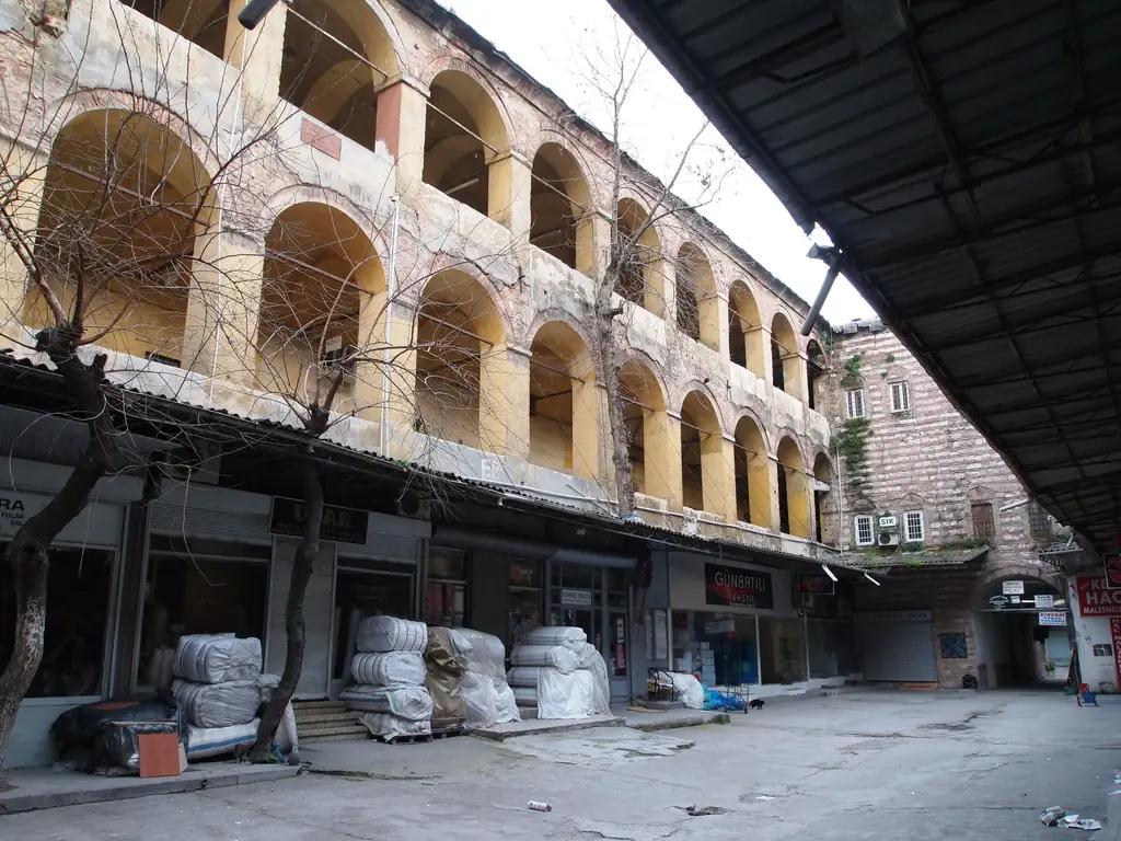 Büyük Yeni Han'ın sokak cephesi; dükkânların üstünde iki sıra kemerli açıklık, üç kat yüksekliğinde duvar, kaldırımda balyalar.