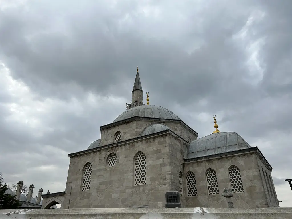 Şemsi Paşa Camii; kesme taş duvarlar, büyük kubbe, minare, yanda daha küçük türbe kubbesi ve bulutlu gök.