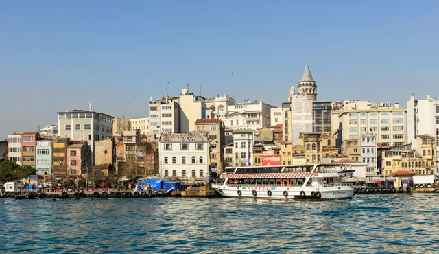 Haliç'ten Karaköy kıyısı; rıhtım boyunca renkli binalar, iskelede beyaz bir yolcu teknesi ve yamacın üstünde Galata Kulesi.