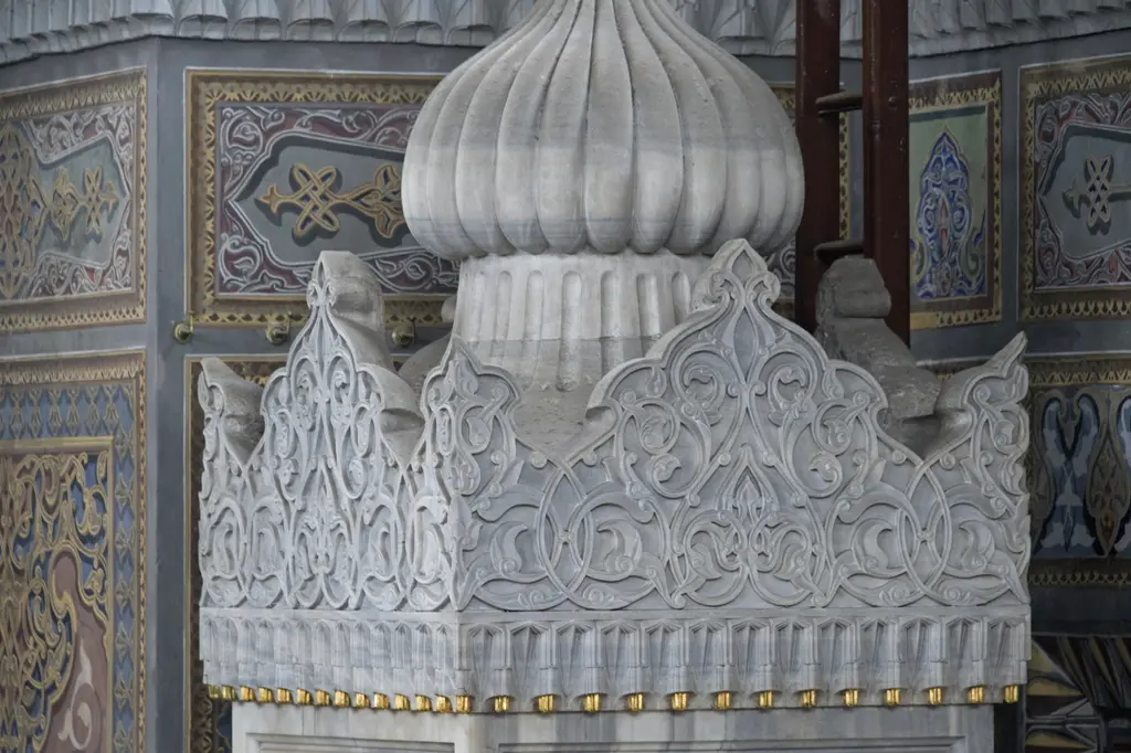 Pertevniyal Valide Sultan Camii'nin mermer minberinin tepesi; dilimli küçük kubbe, oyma süslü mermer taç ve arkada kalem işli duvar.