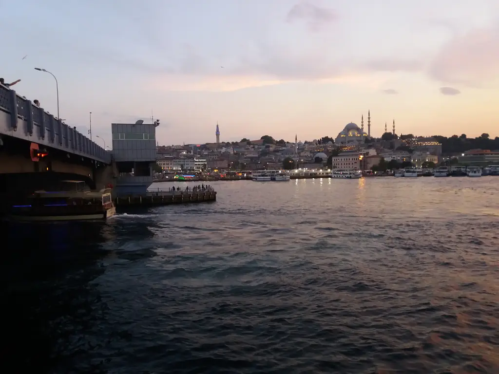 Akşamüstü köprüden Haliç; solda köprünün gövdesi, gri su ve ufukta tarihi yarımadanın siluetiyle pembe gökyüzü.