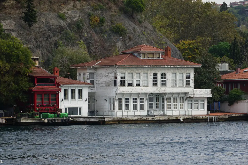 Kadri Paşa Yalısı; geniş beyaz ahşap cephe, kiremit çatı, solda küçük kırmızı köşk ve arkada yamaç.