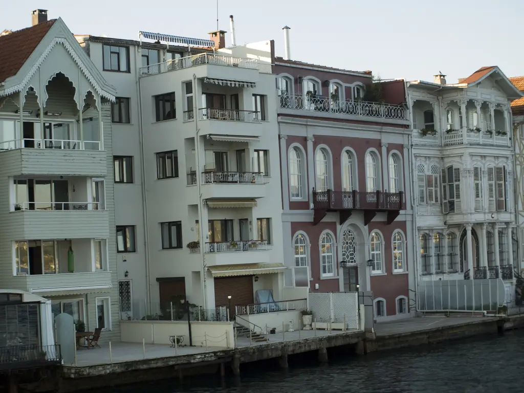 Yeniköy kıyısında yalılar ve apartman; yeşil ahşap cephe, kırmızı tuğla renkli yalı ve suya inen rıhtım.