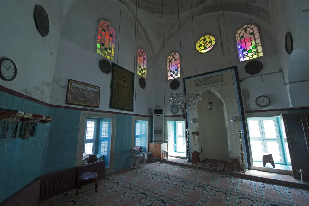 Fethiye Camii'nin cami bölümünde duvar; turkuaz boyalı yüzey, üst sırada renkli camlı kemerli pencereler, altta ahşap dolaplar ve halı.