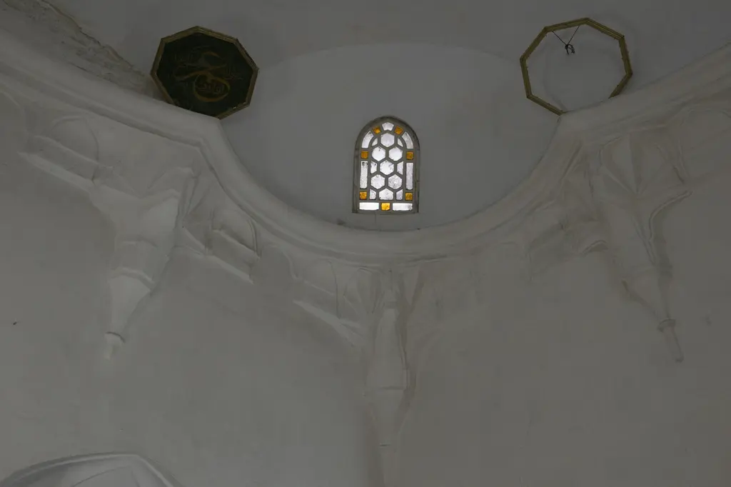 Rum Mehmed Paşa Camii'nde kubbeye geçiş; beyaz sıvalı kemer, mukarnas dilimleri, renkli camlı pencere ve hat madalyonları.