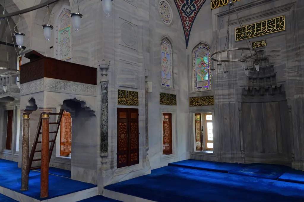 Azapkapı Sokullu Mehmed Paşa Camii'nde kıble duvarı; mukarnaslı mermer mihrap, solda ahşap korkuluklu mahfil, renkli camlar ve yaldızlı yazılar.