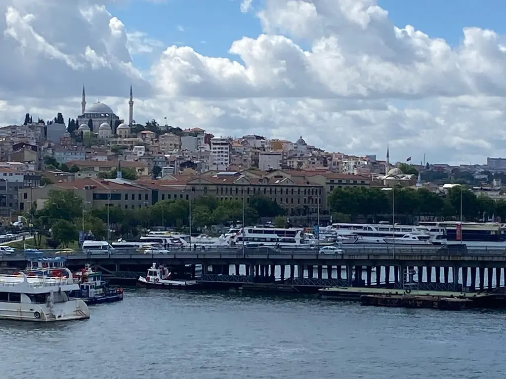 Haliç'ten Cibali kıyısı; önde Atatürk Köprüsü ve tekneler, kıyıda uzun fabrika binası, tepede iki minareli kubbeli cami ve bulutlu gök.