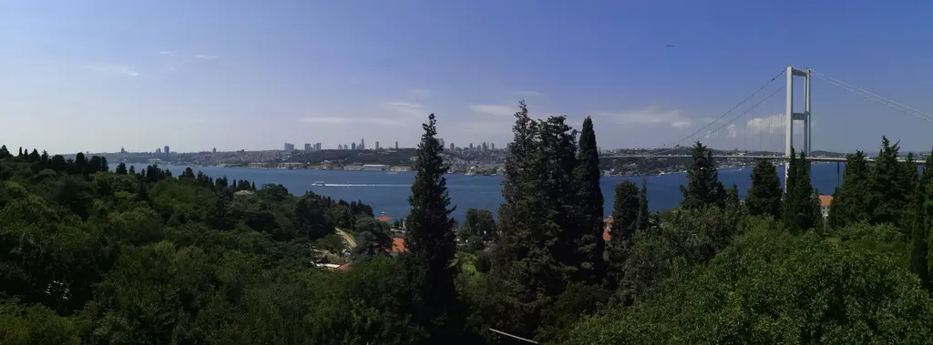 Mihrabat Tabiat Parkı'ndan geniş Boğaz panoraması; önde ağaçlık yamaç, ortada mavi su, sağda köprünün kulesi ve uzakta Avrupa yakasının kuleleri.